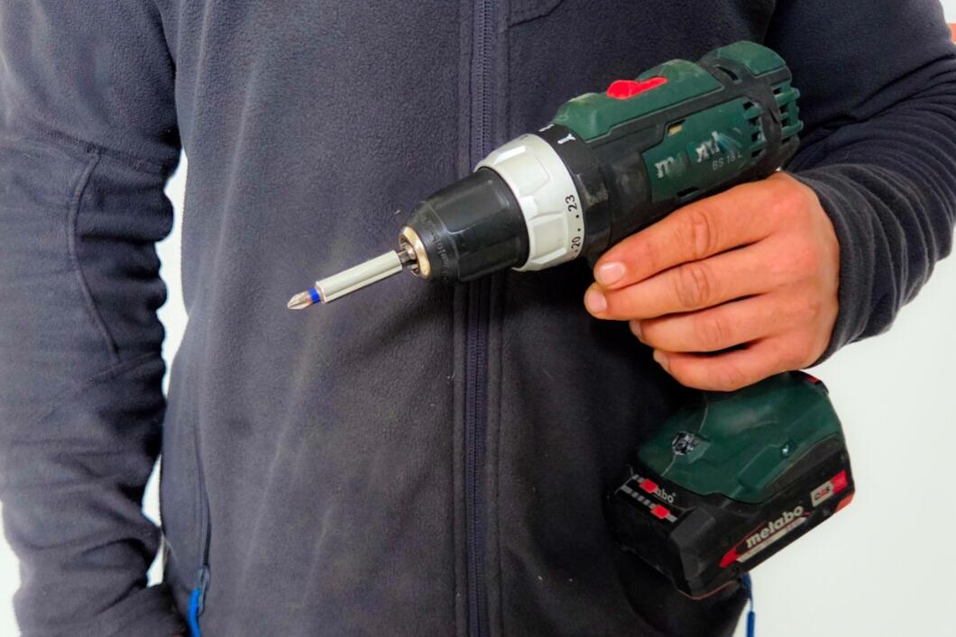 Mitarbeiter in Firmenkleidung mit Akkuschrauber vor einer Reparatur im Objekt