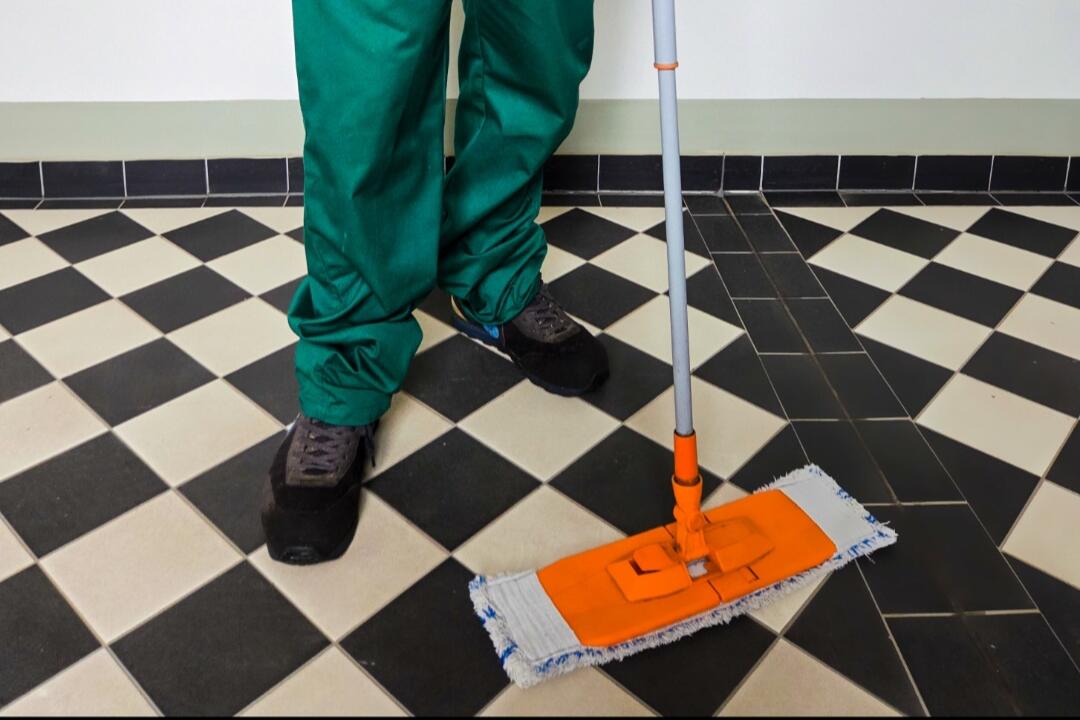 Mitarbeiter in Arbeitskleidung wischt den Fliesenboden im Treppenhaus eines betreuten Objekts