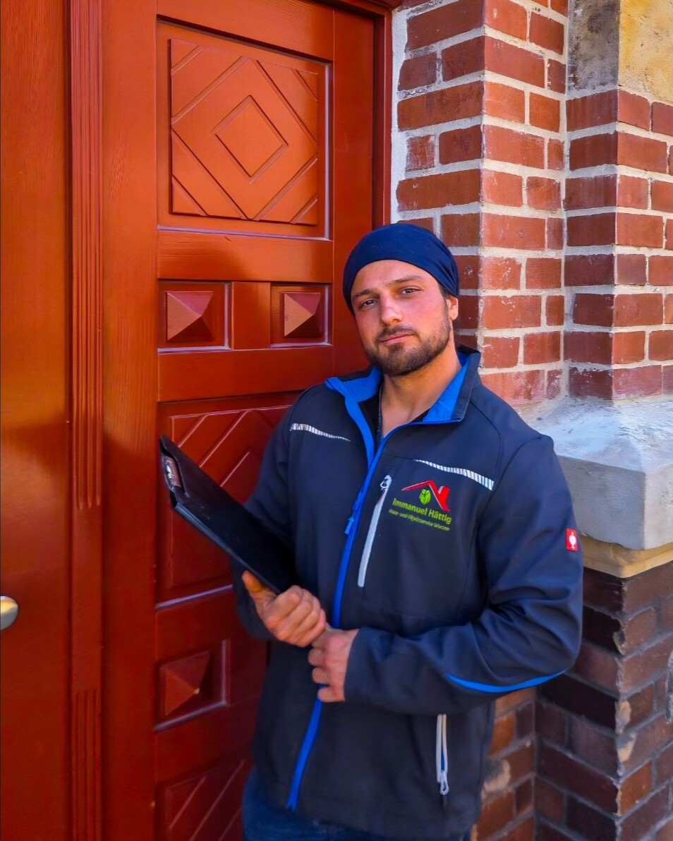 Immanuel Hättig in Arbeitsjacke mit Firmenlogo vor dem Hauseingang eines betreuten Objekts